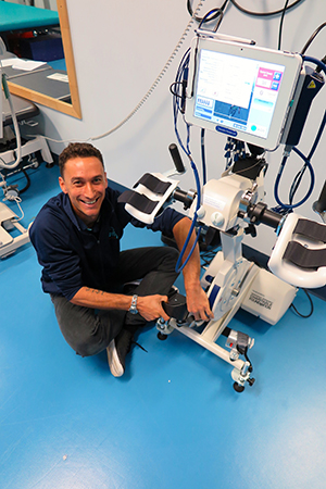 NeuroMoves exercise physiologist Sam Mitchell with the RT300 Functional Electrical Stimulation Ergometer that assists with arm and leg rehabilitation for patients with illnesses such as paraplegia, quadriplegia and stroke.