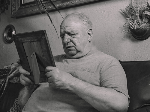 A Grayscale Photo of an Elderly Man Holding a Wooden Frame